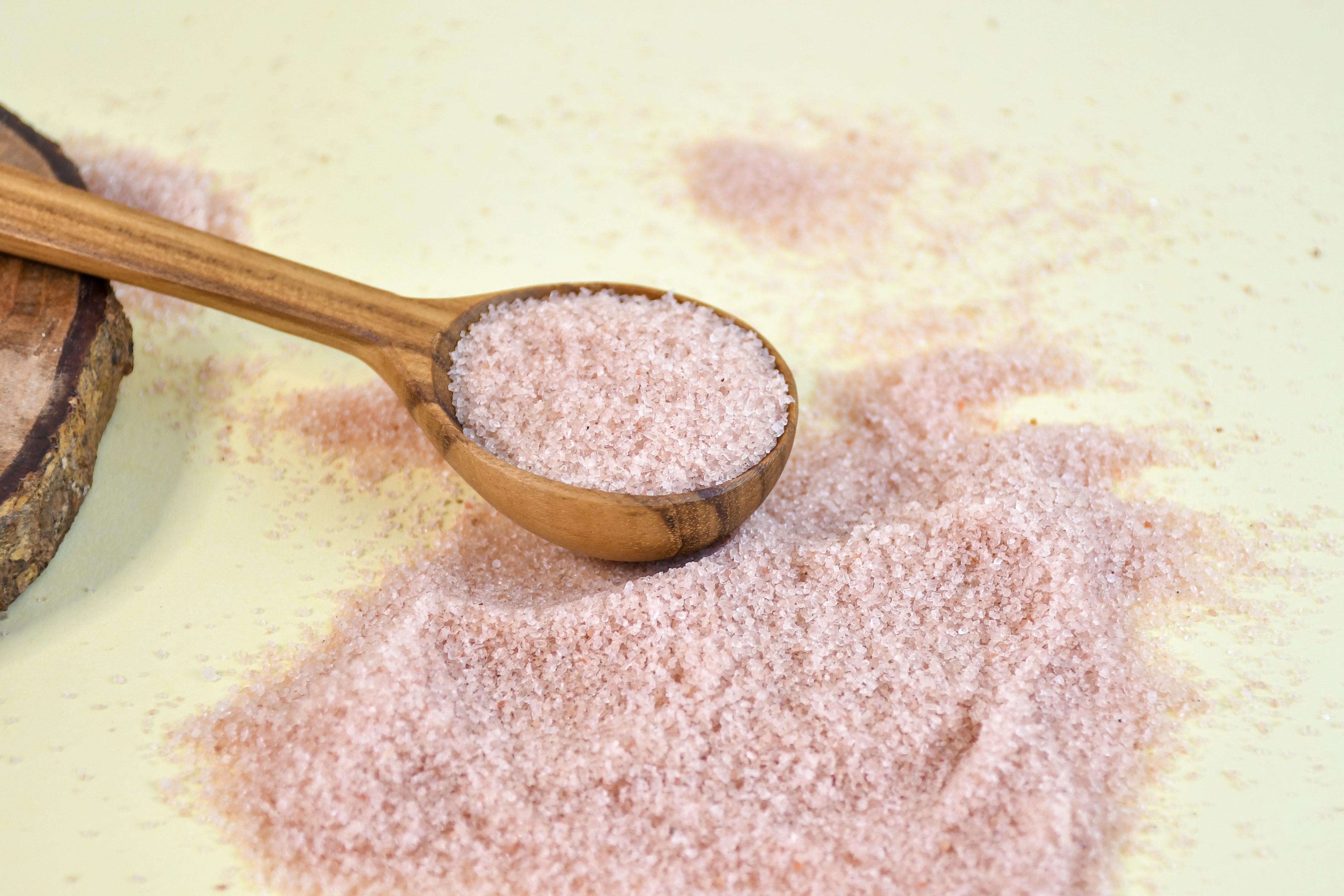 Close-up of pink Himalayan salt in a wooden spoon on a yellow background, highlighting texture.